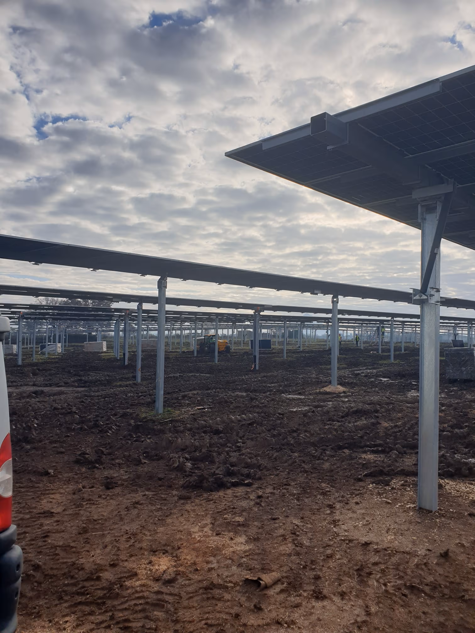 View from under the panel rows during construction, with a tractor working in the background